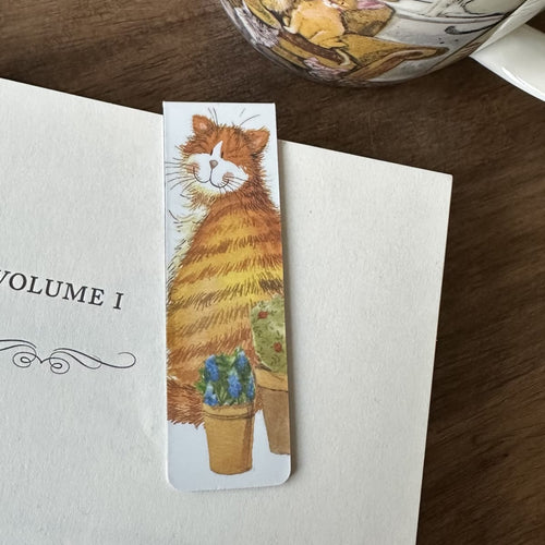 Alex Clark Cat & Pot magnetic bookmark clipped onto the page of an open book, showing how the magnetic bookmark securely holds its place.

