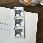 Alex Clark Little Treacle magnetic cat bookmark clipped onto the page of an open book, showing how the magnetic bookmark securely holds its place.