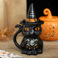 Frightful Folk witchy black cat Halloween lidded mug with pointed hat, orange eyes and floral details beside an orange pumpkin decoration