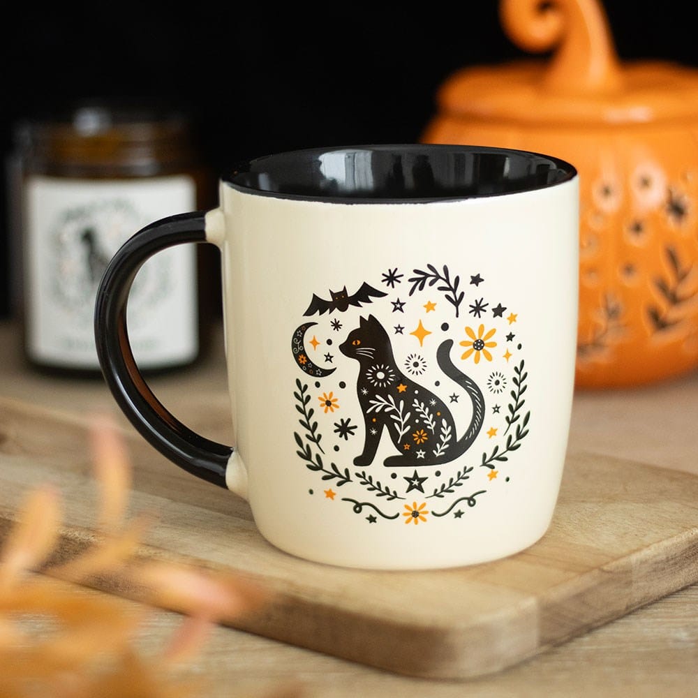 Frightful Folk mystical black cat Halloween mug with crescent moon, bat, stars and orange flowers styled with an autumn pumpkin decoration