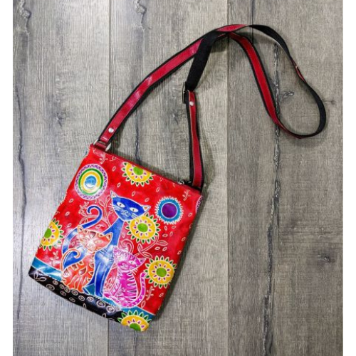 A handmade red leather shoulder bag with a colorful pattern featuring three cats, an adjustable black strap, and a black cotton mix lining.