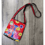 Handmade red leather Three Cats shoulder bag displayed on rustic wooden boards, showing its colourful cat design and adjustable strap.