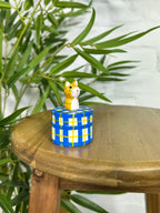 Handmade Fair Trade wooden cat trinket box with ginger tabby lid, displayed on a rustic wooden stool surrounded by green plants.
