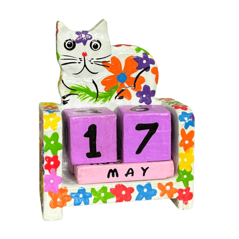 Fair trade handmade wooden cat perpetual calendar featuring a white cat decorated with colourful flowers, purple date blocks and pink month block.