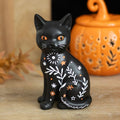 Frightful Folk black cat Halloween ornament with orange eyes, white botanical markings and stars displayed beside an orange pumpkin decoration