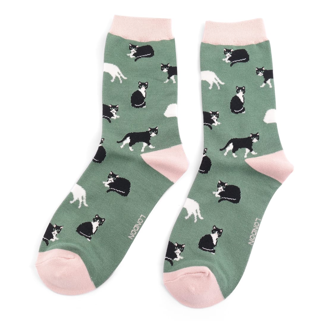 Pair of Miss Sparrow Ladies Bamboo Socks in soft green featuring playful black and white cat silhouettes on a sage green background with pale pink heels, toes and cuffs, made from a soft bamboo-rich fabric.