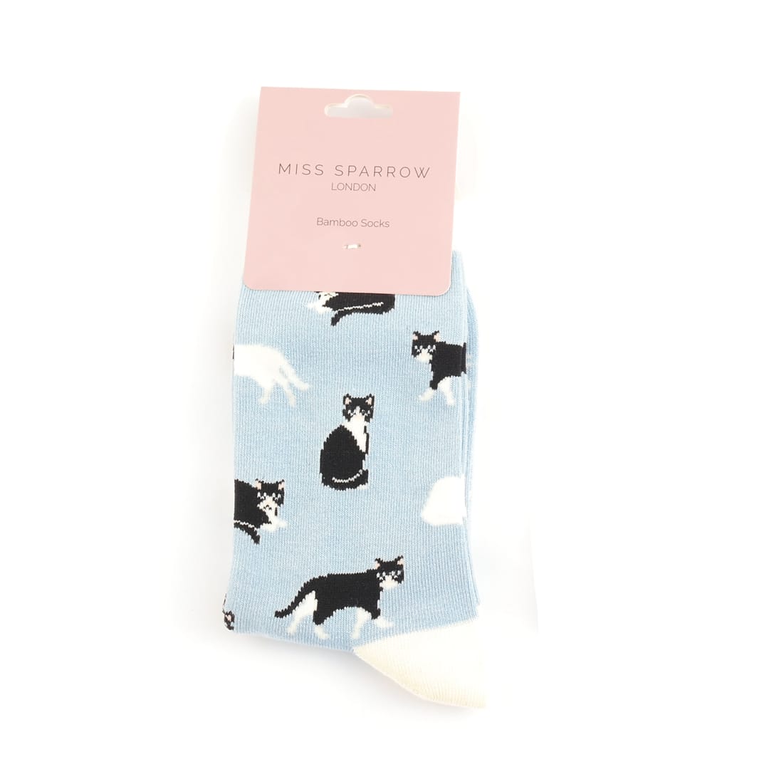 Pair of Miss Sparrow Ladies Bamboo Socks in retail packaging  in powder blue featuring playful black and white cat silhouettes on a soft blue background with cream heels, toes and cuffs, made from a soft bamboo-rich fabric.