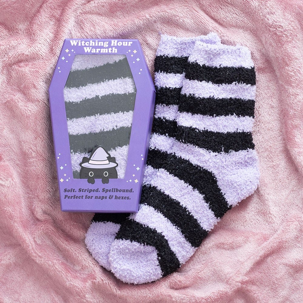 Pastel purple and black striped fluffy Halloween socks with coffin gift box featuring a cute black witch cat, styled on a cosy pink blanket