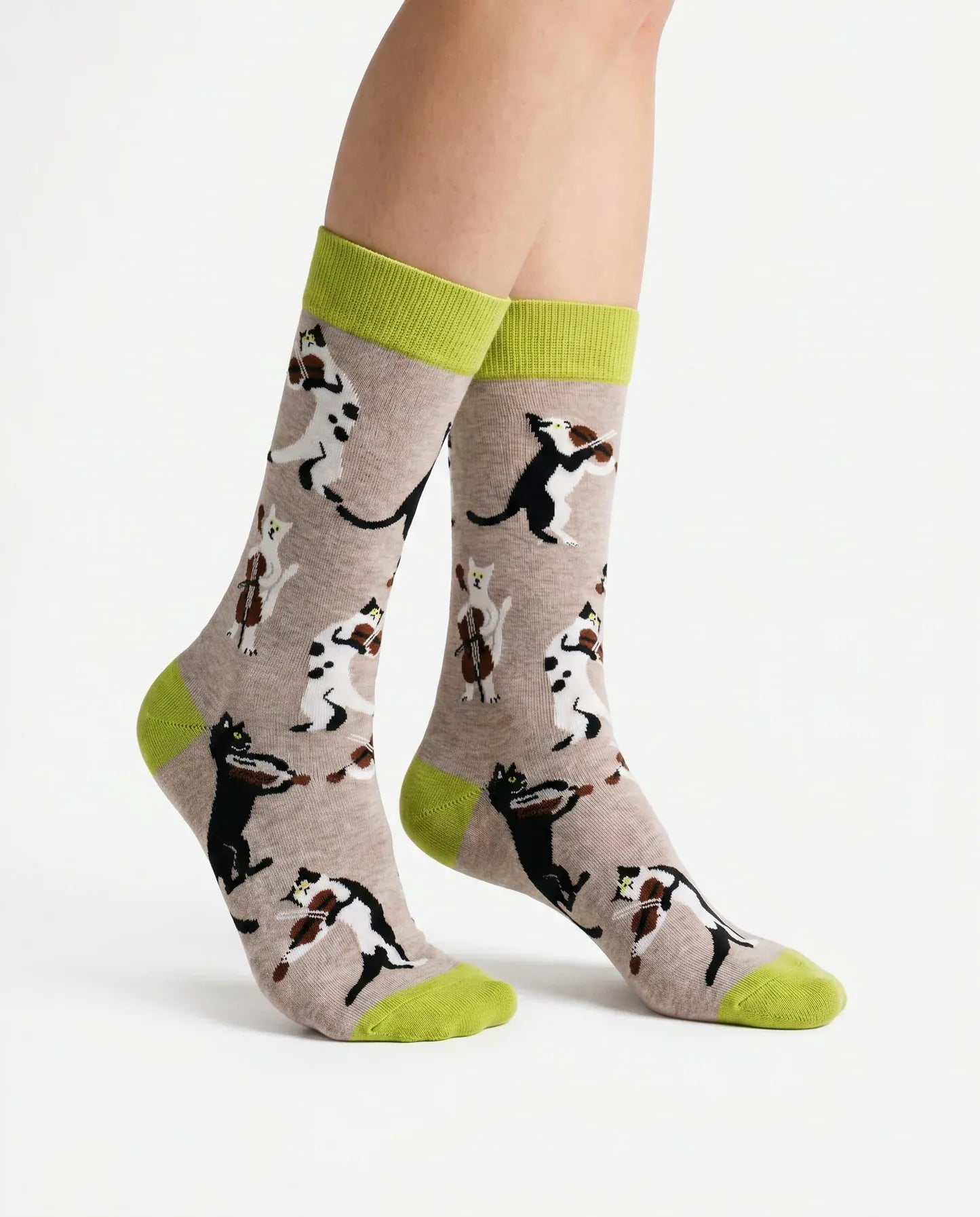 Model wearing Socktopus String Quartet cat socks featuring musical cats playing violins and cello on a soft grey background with lime green cuffs and toes.
