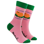 Pair of Socktopus Ladies It's Too Peopley Outside cat socks showing a ginger cat curled up on a green cushion, blue slogan lettering, pink fabric and contrasting green cuffs, heels and toes.