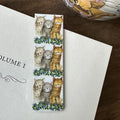 Alex Clark Three Amigos magnetic cat bookmark clipped onto the page of an open book, showing how the magnetic bookmark securely holds its place.
