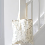 White cat print polycotton tote shopping bag hanging from a stair rail, showing its long handles and playful feline design