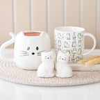 White cat shaped ceramic mug displayed alongside illustrated cat mug and ceramic cat ornaments, gift ideas for cat lovers.