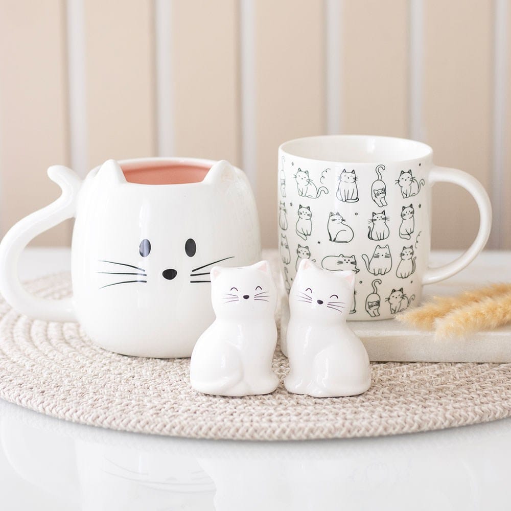 White cat shaped ceramic mug displayed alongside illustrated cat mug and ceramic cat ornaments, gift ideas for cat lovers.